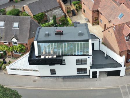 A modern white house with a glass roof and balcony next to brick houses at Castle View in Warwick