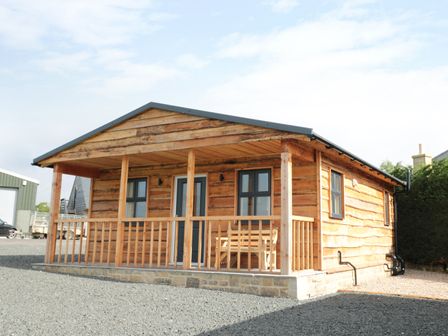 A wooden cabin with a front porch and railing at Breamish in Longframlington