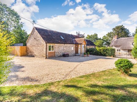 A stone house with a tiled roof and gravel driveway surrounded by green trees at Old Farm Stables South Barrow near Sparkford