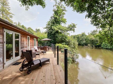A wooden deck with lounge chairs and a dining table overlooking a river at 6 Water's Edge in Lanreath