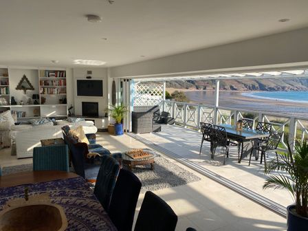 A living room with sofas a chess table and an outdoor dining area overlooking the beach at The Sandcastle in Freshwater East