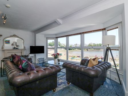 A living room with two leather sofas a glass coffee table a floor lamp and large windows overlooking a waterfront at Sea View apartment in Borth-Y-Gest