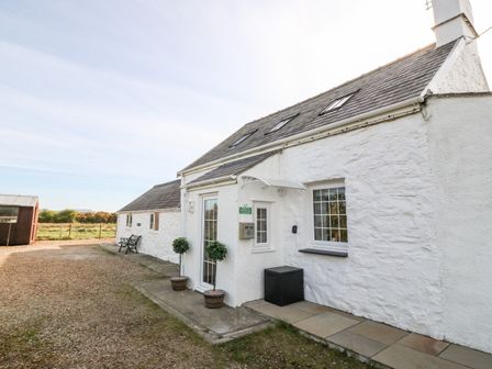 The exterior of a white stone house with potted plants by the door and a bench on the side at Min-y-rhos in Edern