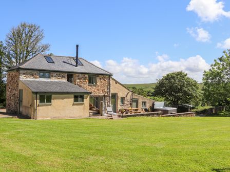 A stone and plaster house with outdoor seating and a hot tub on a grassy lawn at Sunbury Barn in St Agnes