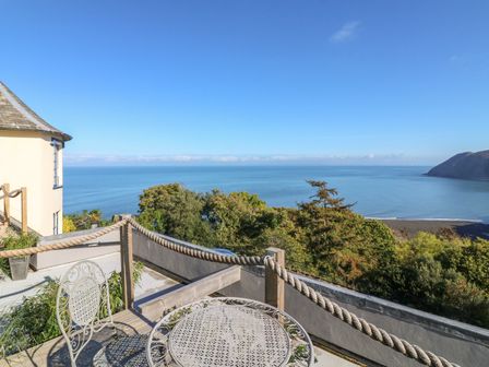 A balcony with metal table and chairs overlooking the sea and trees at C S Lewis Balcony in Lynton