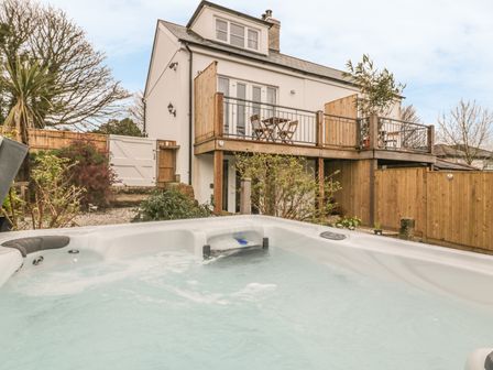 An outdoor hot tub with a two story house with a balcony and wooden fencing at Crift Farm Cottage Lanlivery near Lostwithiel