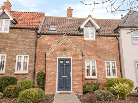 A brick house with a blue door and multiple white framed windows surrounded by shrubs at Bayside Cottage The Bay near Filey