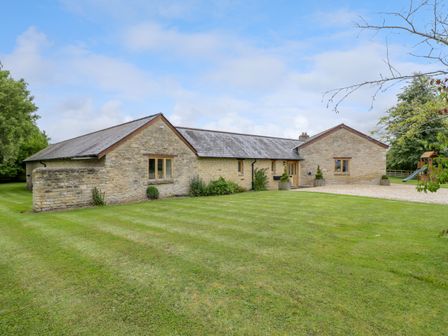 A stone building with a slate roof on a grassy lawn with trees at Lower Farm Barn Aston Near Bampton