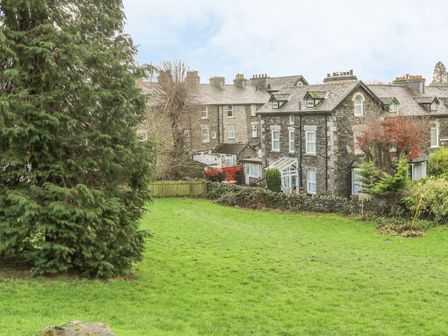 A large grassy garden with trees and stone houses in the background at Giddy Goose in Windermere