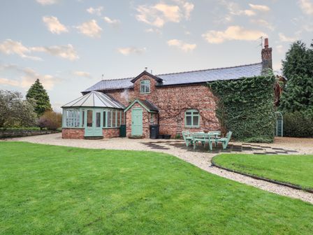 A brick house with a conservatory and outdoor seating on a lawn at The Coach House in Llanymynech