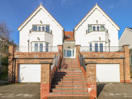A white two-story house with twin gables and a central staircase leading to the front door with garages below at Seashells in Tenby