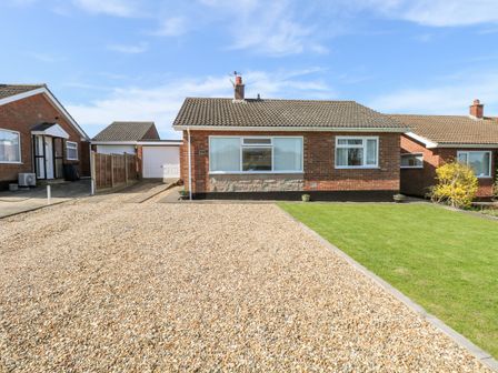 A brick bungalow with a gravel driveway and a lawn at Elliotts Retreat in Sheringham