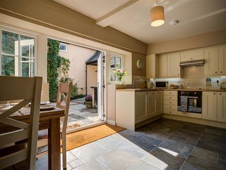 A kitchen with cream cabinets and tiled floor opening to a patio with plants at Mill Race in Burford