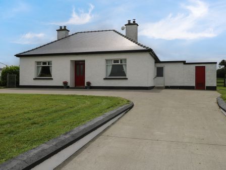 A single-story house with white walls red doors and windows a driveway and a lawn at Kates Cottage near Ballina County Mayo