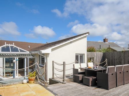 An outdoor deck area with a dining table and chairs next to a white house at Coastal Haven in Crackington near Crackington Haven