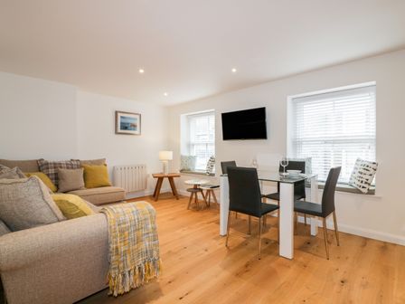 A living room with sofas, dining table, chairs, windows with blinds and cushions at Midships in Mevagissey
