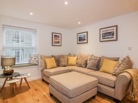 A living room with a beige sectional sofa with cushions and framed pictures on the wall at Captain's Cabin in Mevagissey