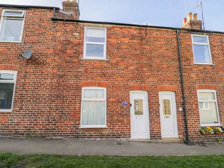 A brick exterior of a row of houses with white doors and windows at Sea Breakers Cottage in Filey