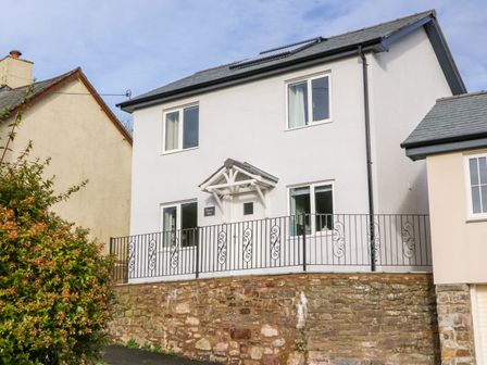A two-story house with white walls and a black wrought iron railing on a stone foundation at Exmoor View in North Molton