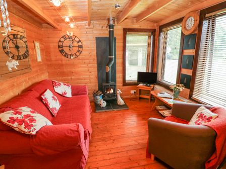 A wooden living room with a red sofa and armchair a wood stove and a small TV at The Lodge in Rosemarket