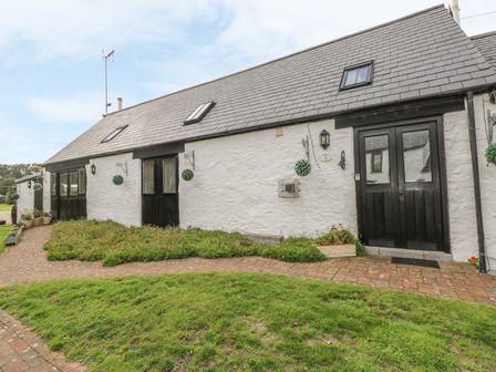 A white cottage with black doors and windows and a sloped roof surrounded by grass and plants at Heather Cottage in Rosemarket