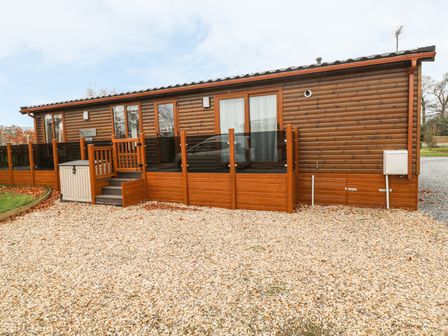 A wooden lodge with glass doors and windows surrounded by a gravel driveway at Avonal Lodge (24) in Dunning