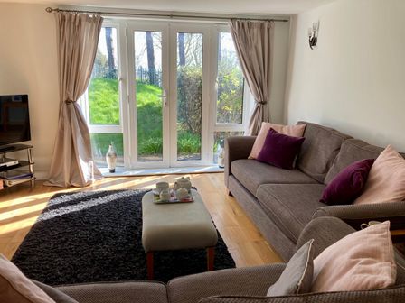 A living room with sofas and cushions near glass doors with curtains and a rug at Admirals Retreat in Weymouth