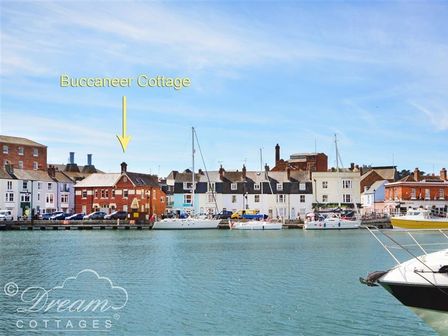 A waterfront with boats and buildings including Buccaneer Cottage at Brewers Quay Harbour