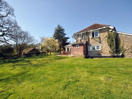 A stone house with a brick extension and outdoor seating on a lawn with trees at Culverwells in Axminster