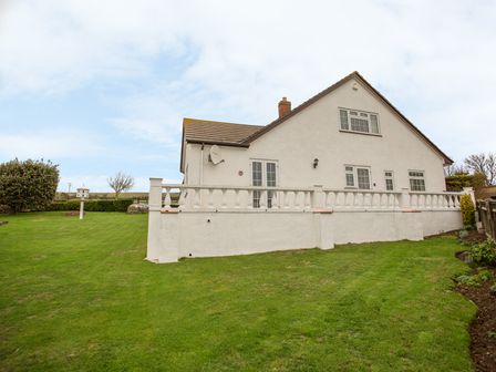 A white house with a tiled roof and fenced patio overlooking a lawn with a birdhouse at The Doves in Burton Bradstock