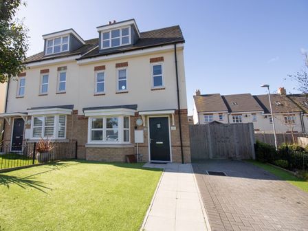 A front view of a three-story end terrace house with a lawn and driveway at The Ferns in Weymouth