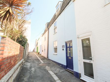 A narrow street with houses on the right and a brick wall with plants on the left at Firkin Cottage Brewers Quay Harbour