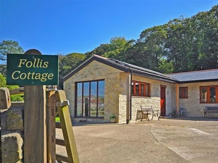 An exterior view of a stone cottage with benches and a gate with a Follis Cottage sign in Nottington
