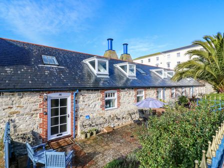 Exterior view of a stone and brick house with multiple windows and blue doors a patio with chairs a table and an umbrella and plants at The Gables in Brewers Quay Harbour
