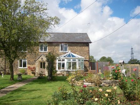 A stone cottage with a glass conservatory and a garden with flowers and trees at Grazeland Cottage in Bridport