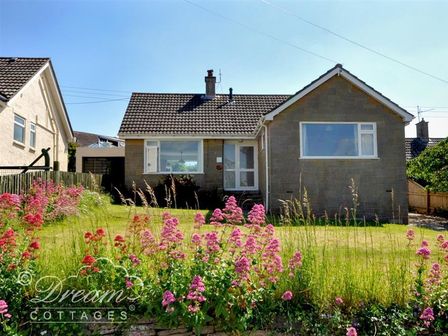 A bungalow with a tiled roof and large windows with a garden with pink flowers and grass at Hillview Bungalow in Burton Bradstock