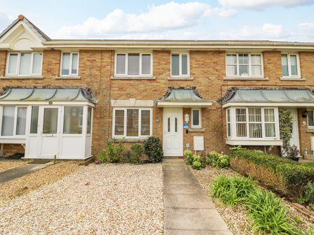 A brick terraced house with a white front door gravel front garden and small plants at Home Waters in Wyke Regis