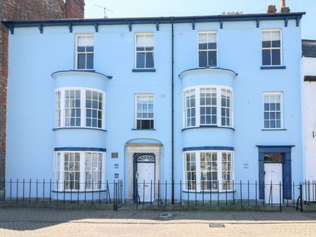 A blue painted two storey building with bay windows and white doors with black railings in front at Harbour Watch Apartment 1 Brewers Quay Harbour