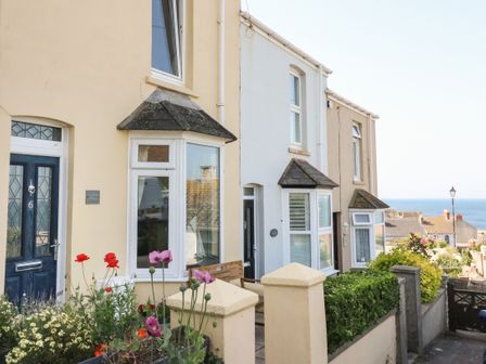 A row of terraced houses with flowers and bushes in front and a view of the sea at Langham Cottage in Portland