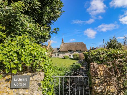 Stone cottage with thatched roof behind a metal gate and garden at Lychgate Cottage Osmington