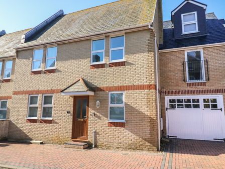 The front exterior of a brick house with several windows a wooden door and a white garage door at Mariners Rest in Weymouth