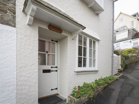 The exterior entrance of a white painted house with a white door and a window with flower beds at 11 Robinsons Row in Salcombe