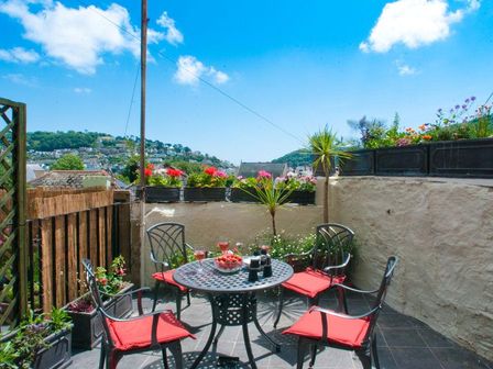 An outdoor patio with a round table and four chairs with red cushions at The Cottage 13 Clarence Hill Dartmouth