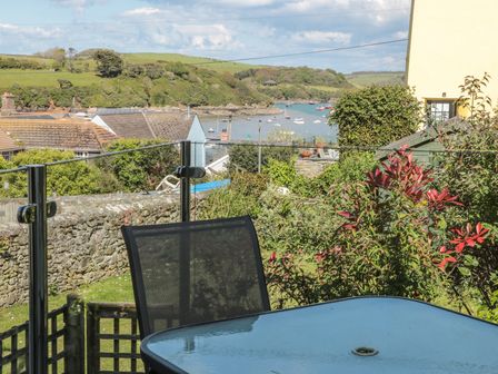 Glass topped outdoor table and chair on a patio with greenery stone wall boats on a river and houses in the background at 14a Courtenay Street Salcombe