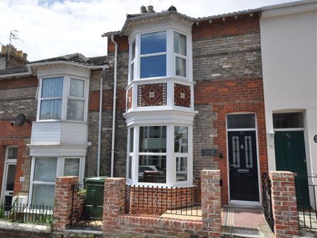 Front view of a brick terraced house with bay windows and a black front door at Pedaller's Cottage in Weymouth