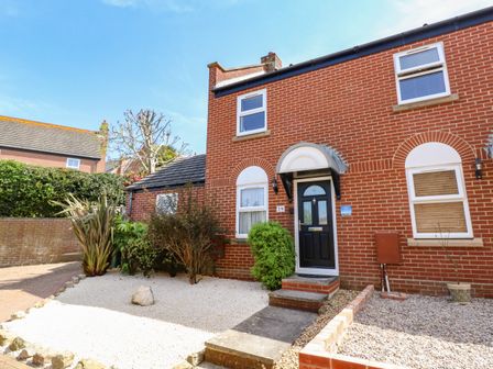 A brick house with a black front door and three windows with gravel and plants in the front garden at The Pines in Weymouth