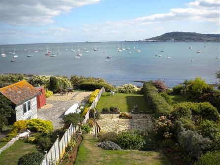 A garden with a shed and patio overlooking a bay with sailboats at Rainbow's End in Cove Castle