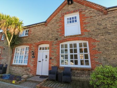 Front view of a brick house with white framed windows a white door two black chairs and a palm tree at Reaver Brewers Quay harbour