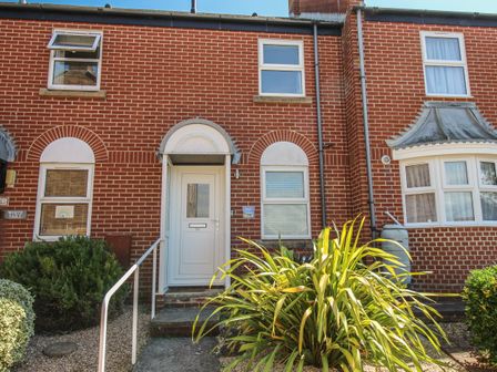 Front of a red brick terraced house with white door and windows and plants in front at Rockpools in Weymouth
