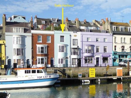 A row of multi-colored buildings along a waterfront with a boat named Top Cat III docked at Safe Harbour Brewers Quay harbour